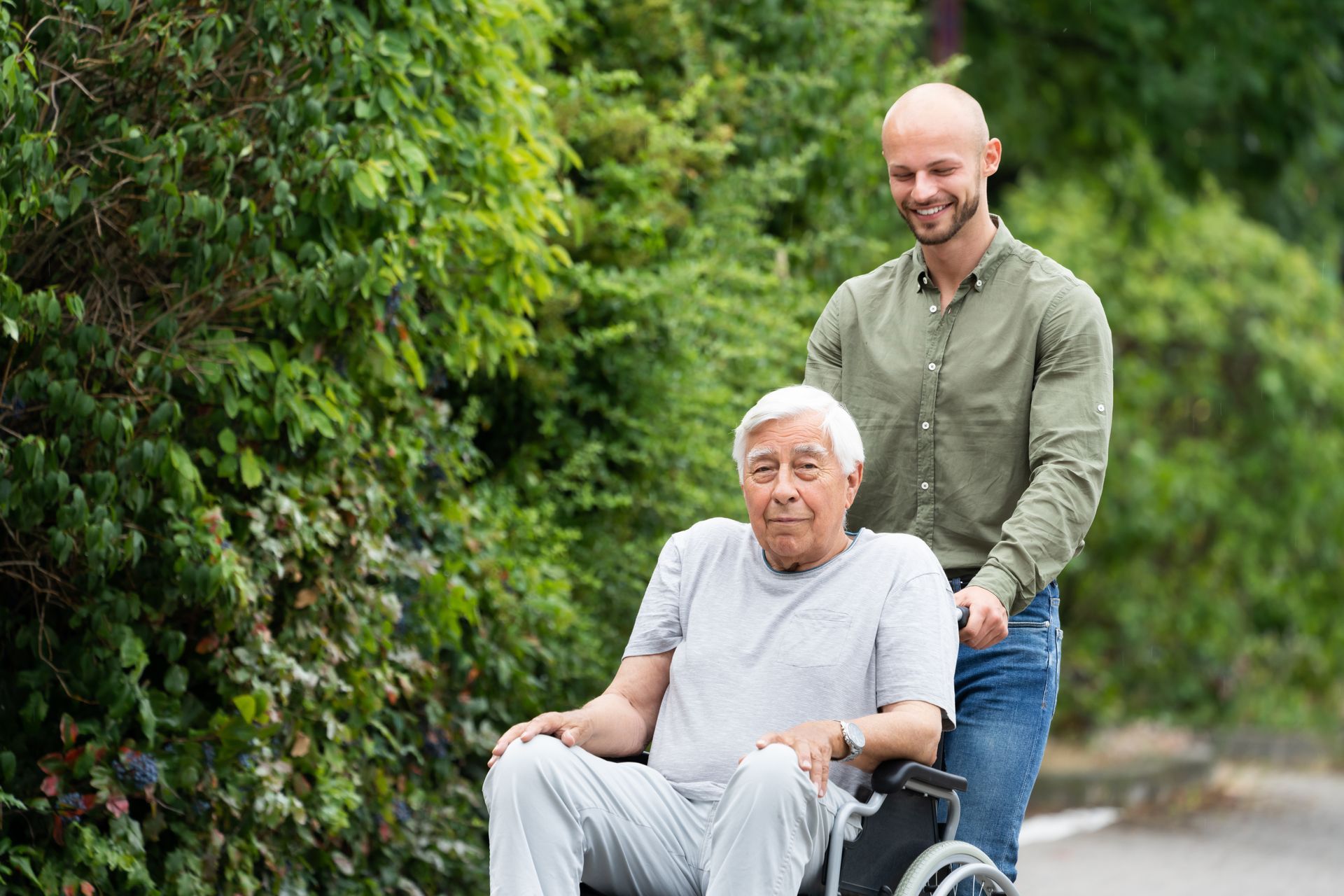 Ein alter Mann im Rollstuhl wird von einem Jüngeren Mann gefahren