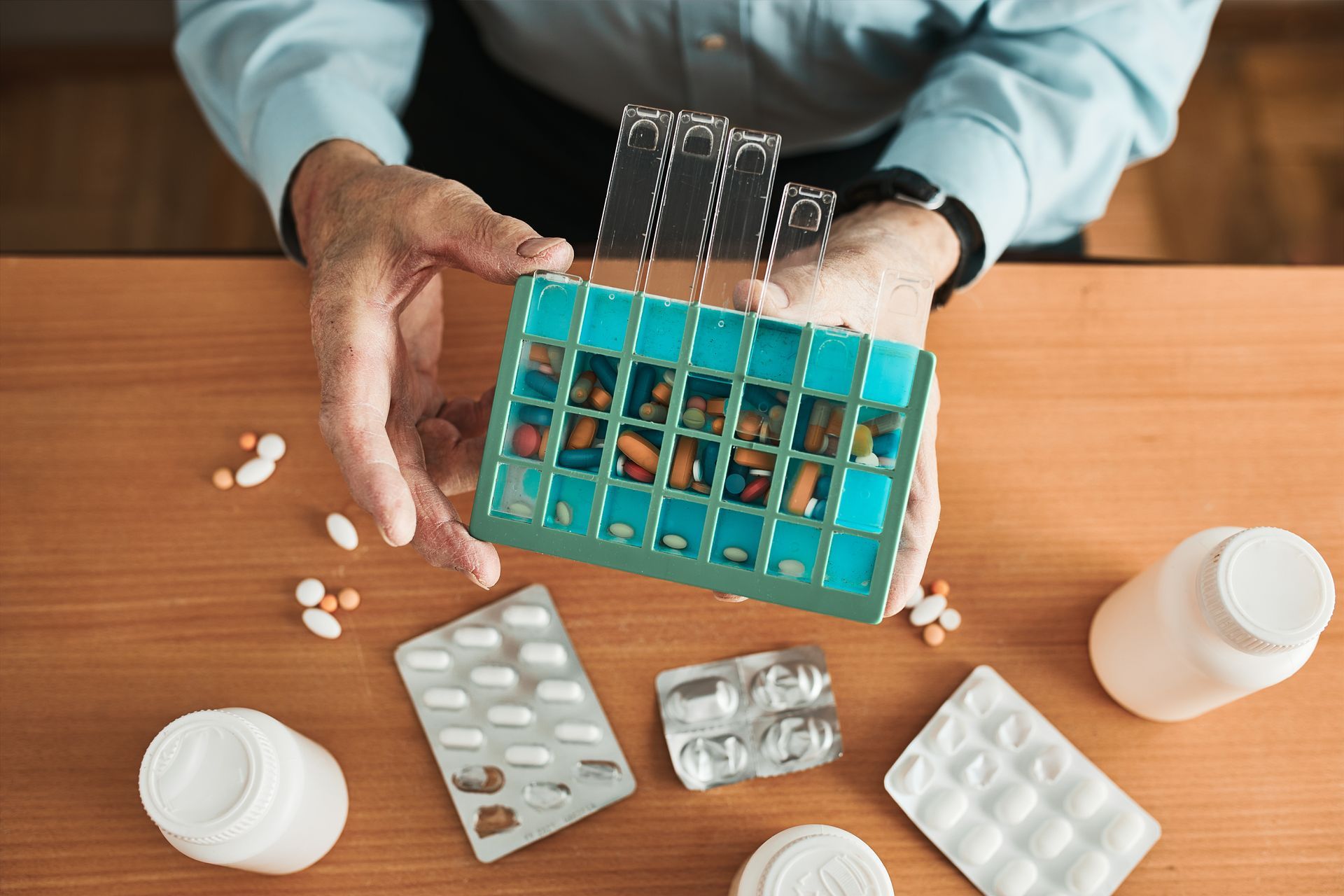 Ein Mann sitzt an einem Tisch und hält eine Pillenschachtel voller Pillen in der Hand.