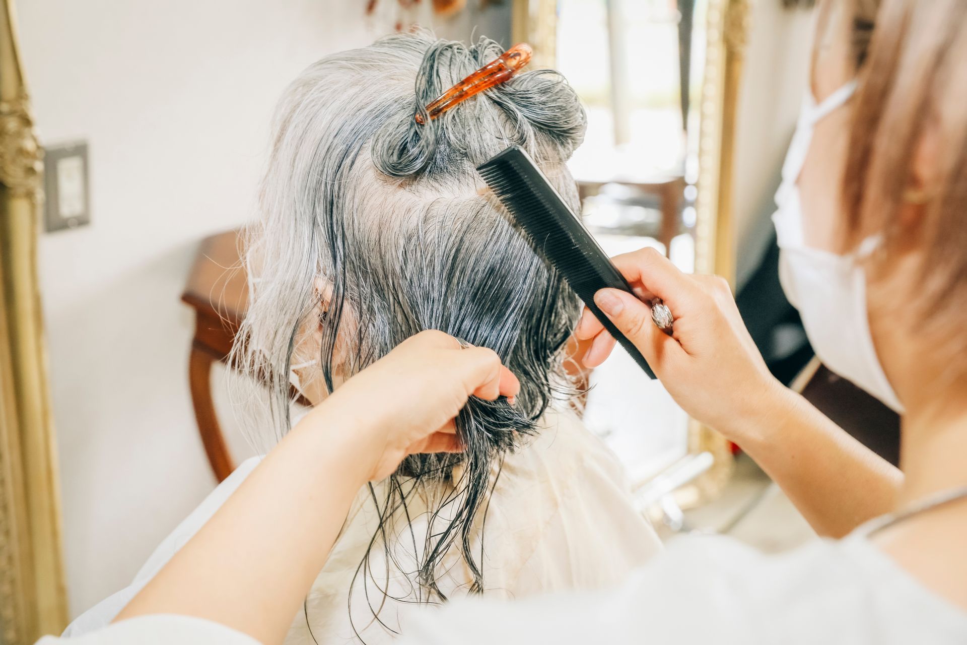 Eine Frau lässt sich von einem Friseur vor einem Spiegel die Haare färben.