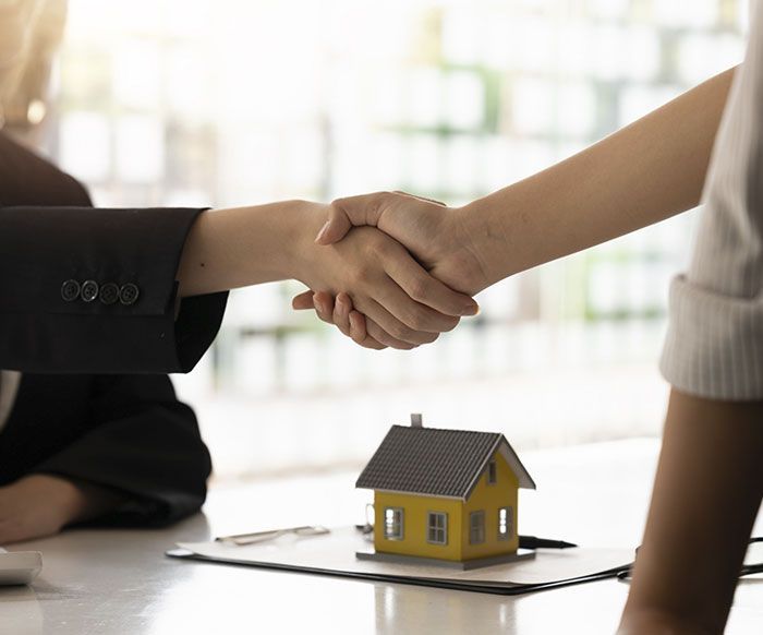 Una mujer le da la mano a un agente inmobiliario frente a una casa modelo.
