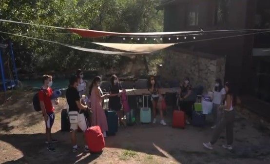 Grupo de personas con equipaje bajo una zona sombreada al aire libre.