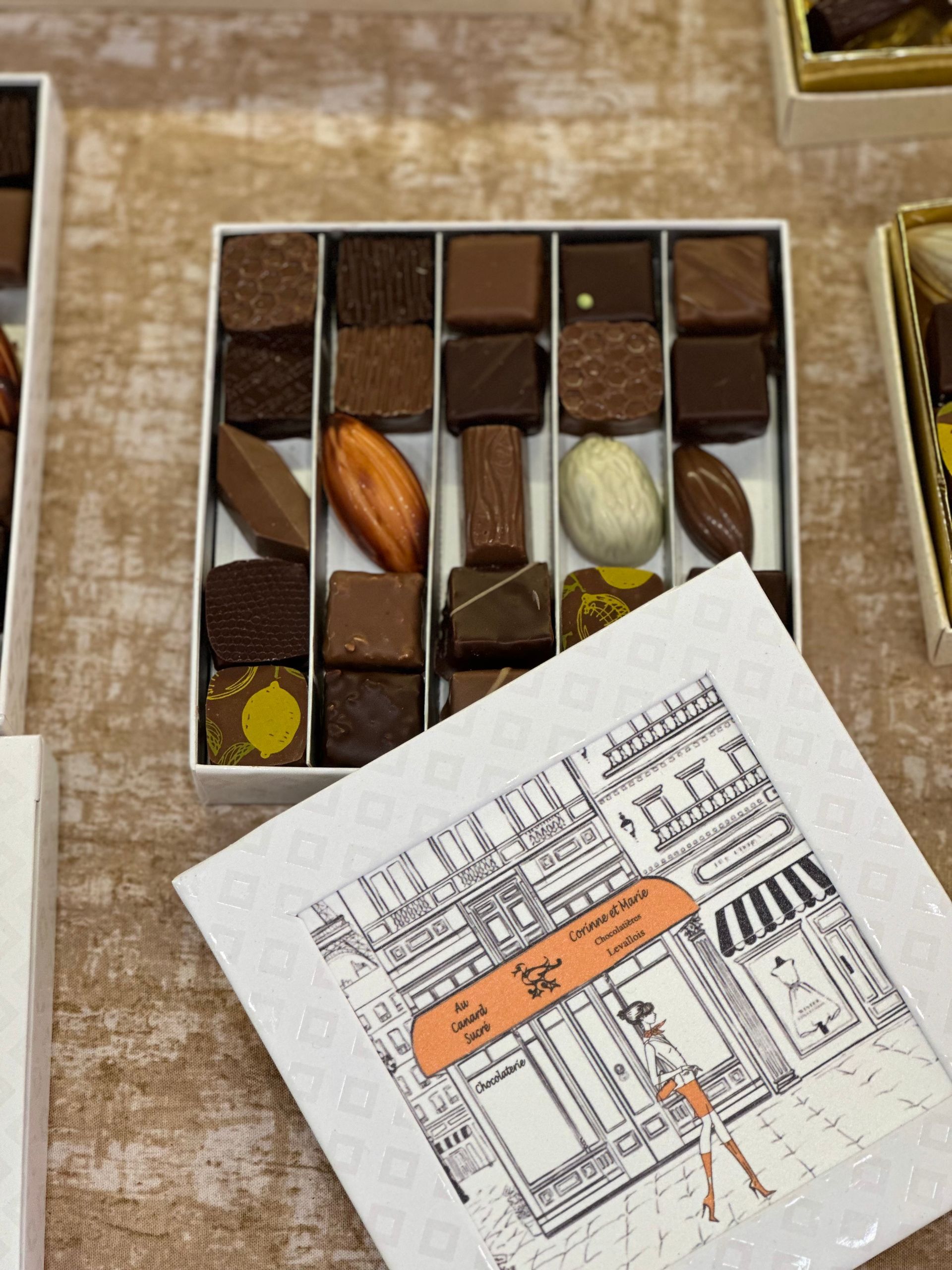 Boîte de chocolats ouverte contenant des chocolats assortis et une petite carte illustrée posées sur une table