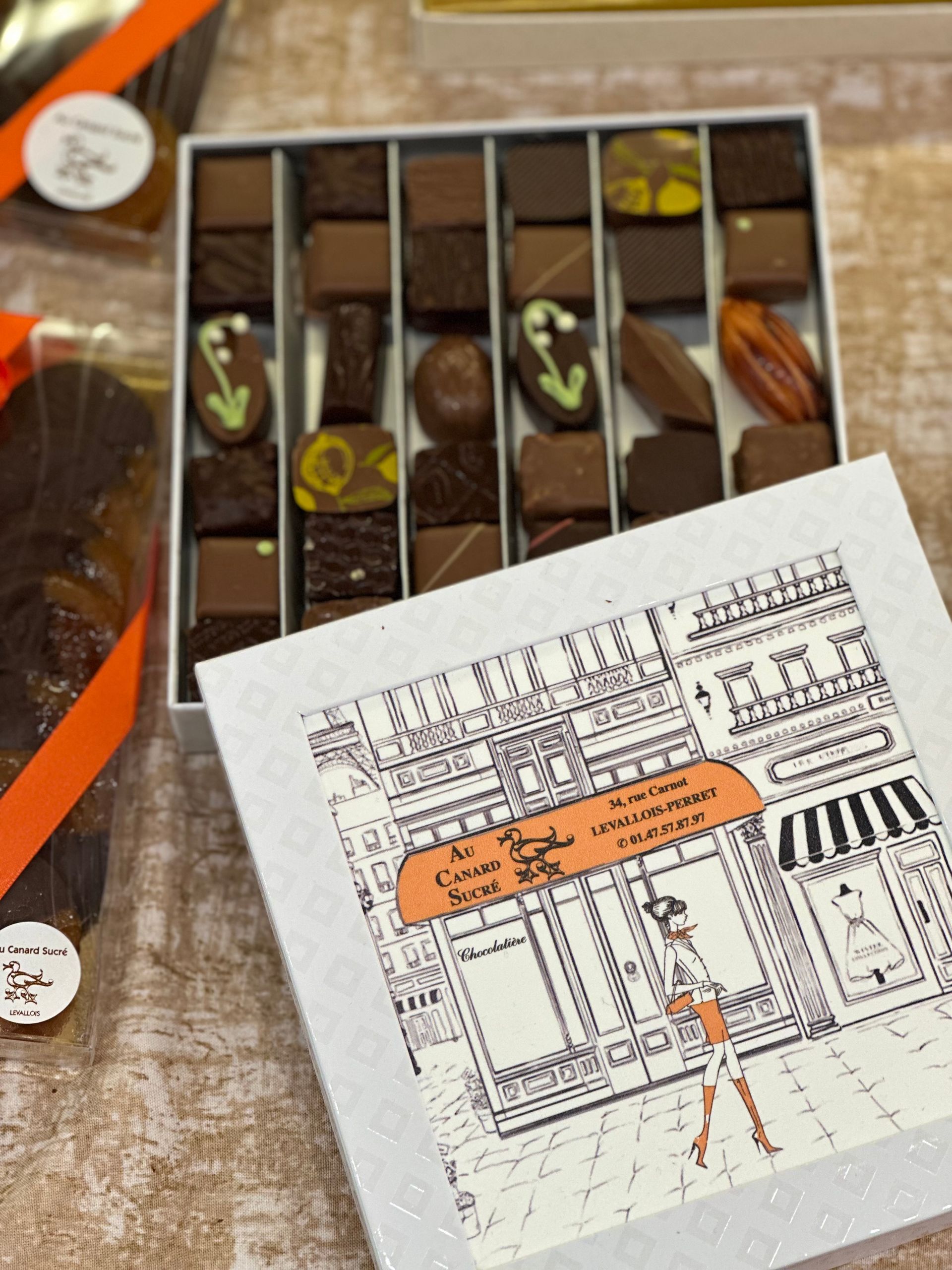 Chocolats assortis dans une boîte, à côté d'une carte illustrée pliée, posée sur une surface en bois.