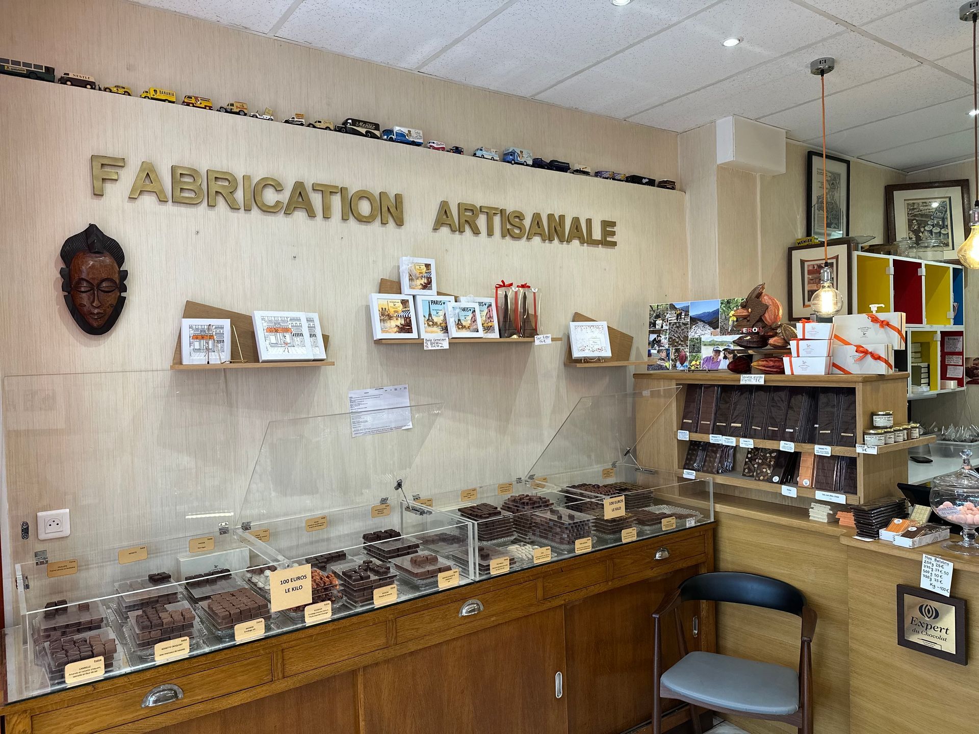 Comptoir de chocolaterie artisanale avec vitrines, étagères et enseigne « fabrication artisanale » au mur