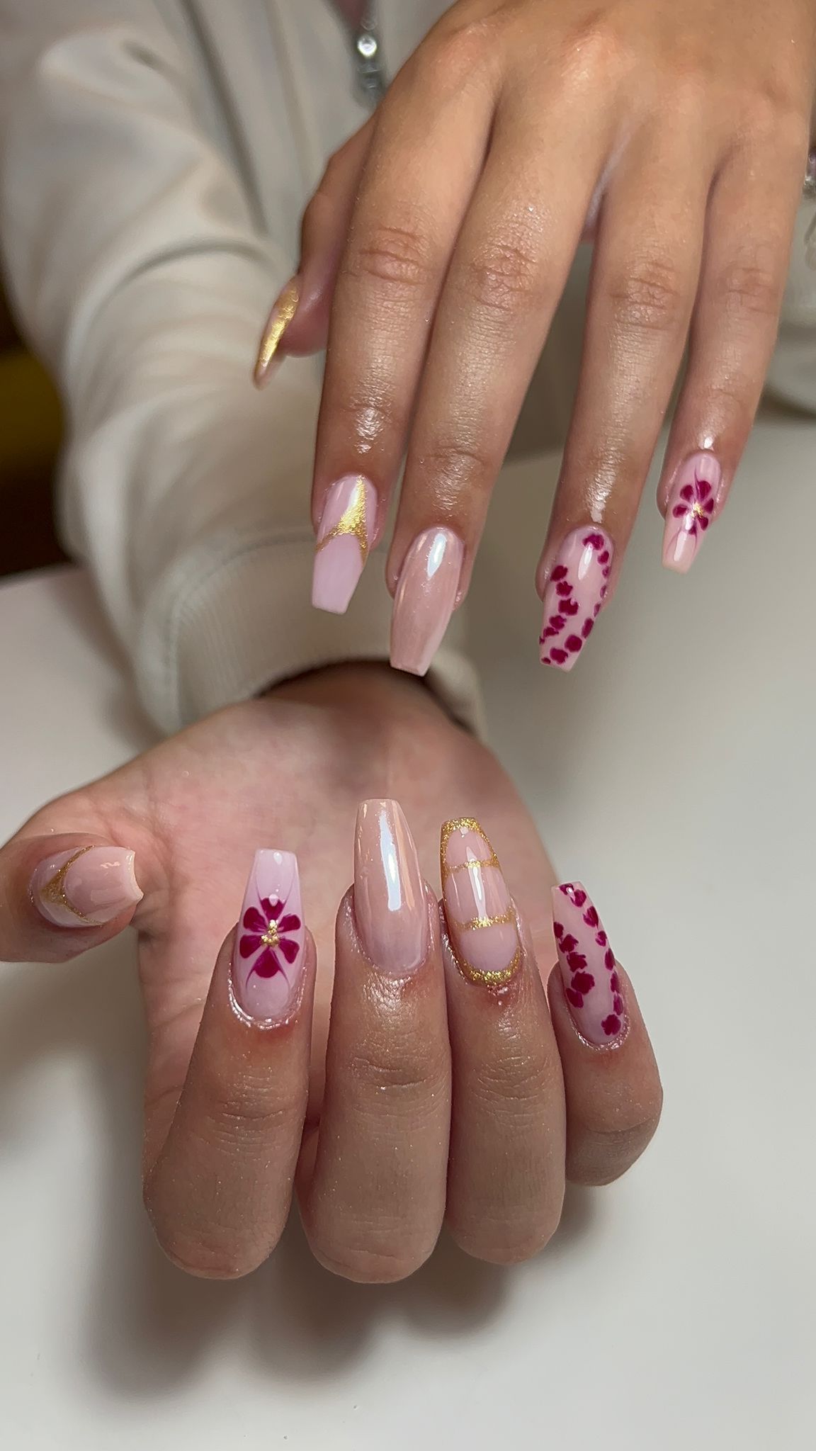 Manos con uñas largas y pulidas. Base rosa con detalles dorados y diseños de corazones rojos.
