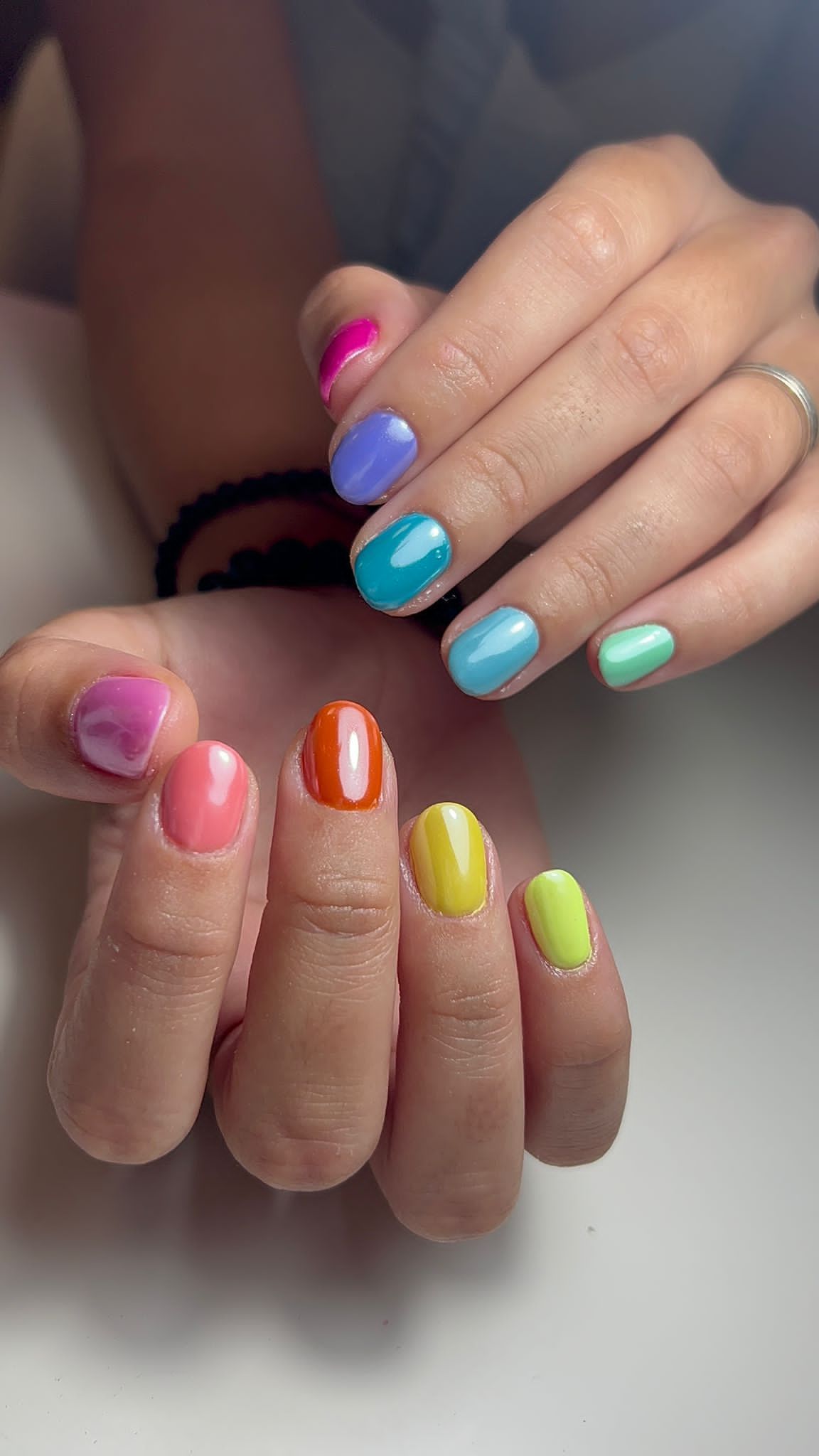 Manos con esmalte de uñas cortas de colores del arco iris: rosa, morado, verde azulado, azul, verde, naranja y amarillo.