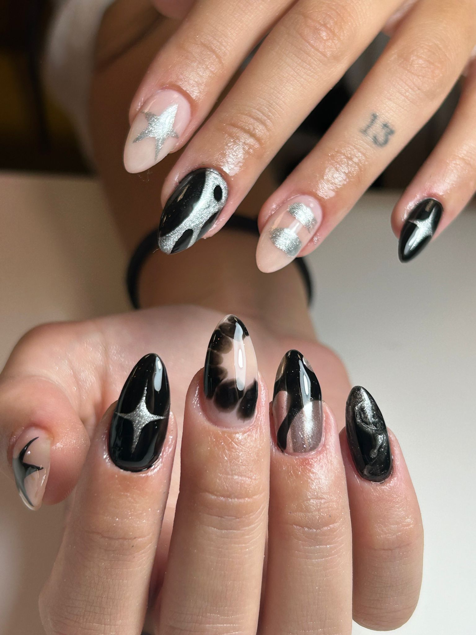 Primer plano de uñas cuidadas con diseños negros y plateados sobre un fondo claro.