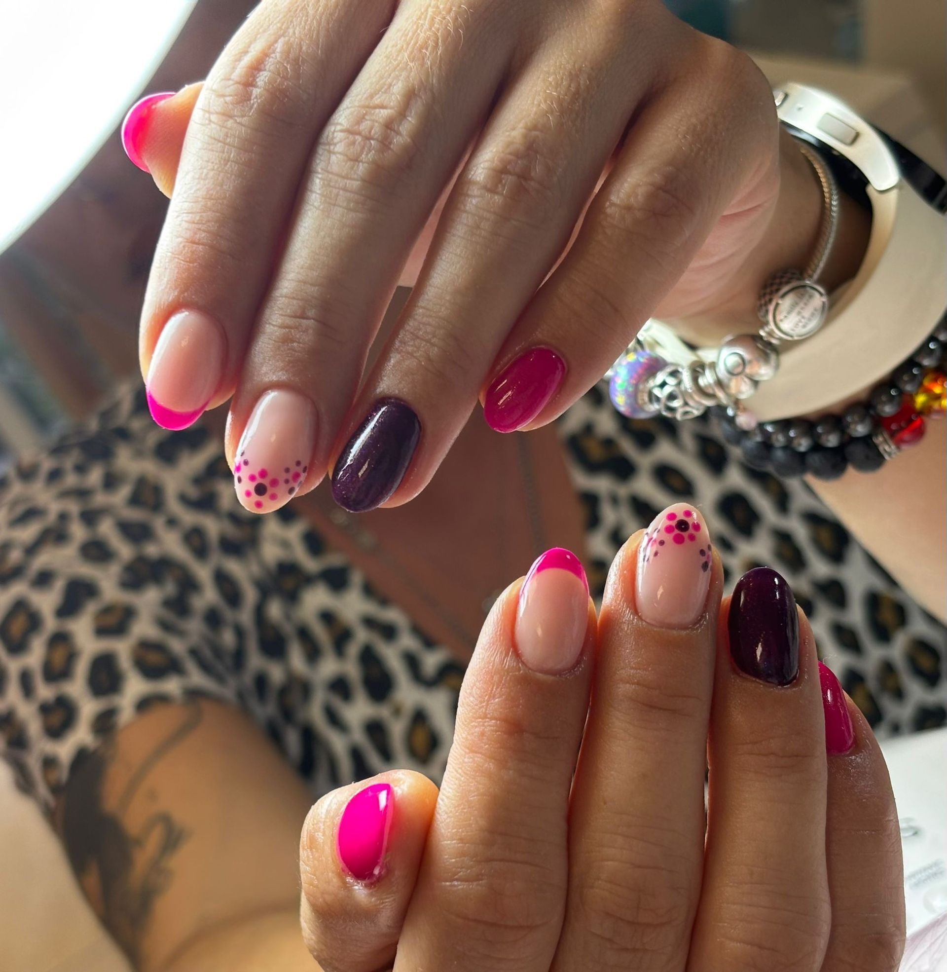 Manos con uñas de forma ovalada, colores rosa y magenta, algunas con diseños de puntos, sobre un fondo de estampado de leopardo.