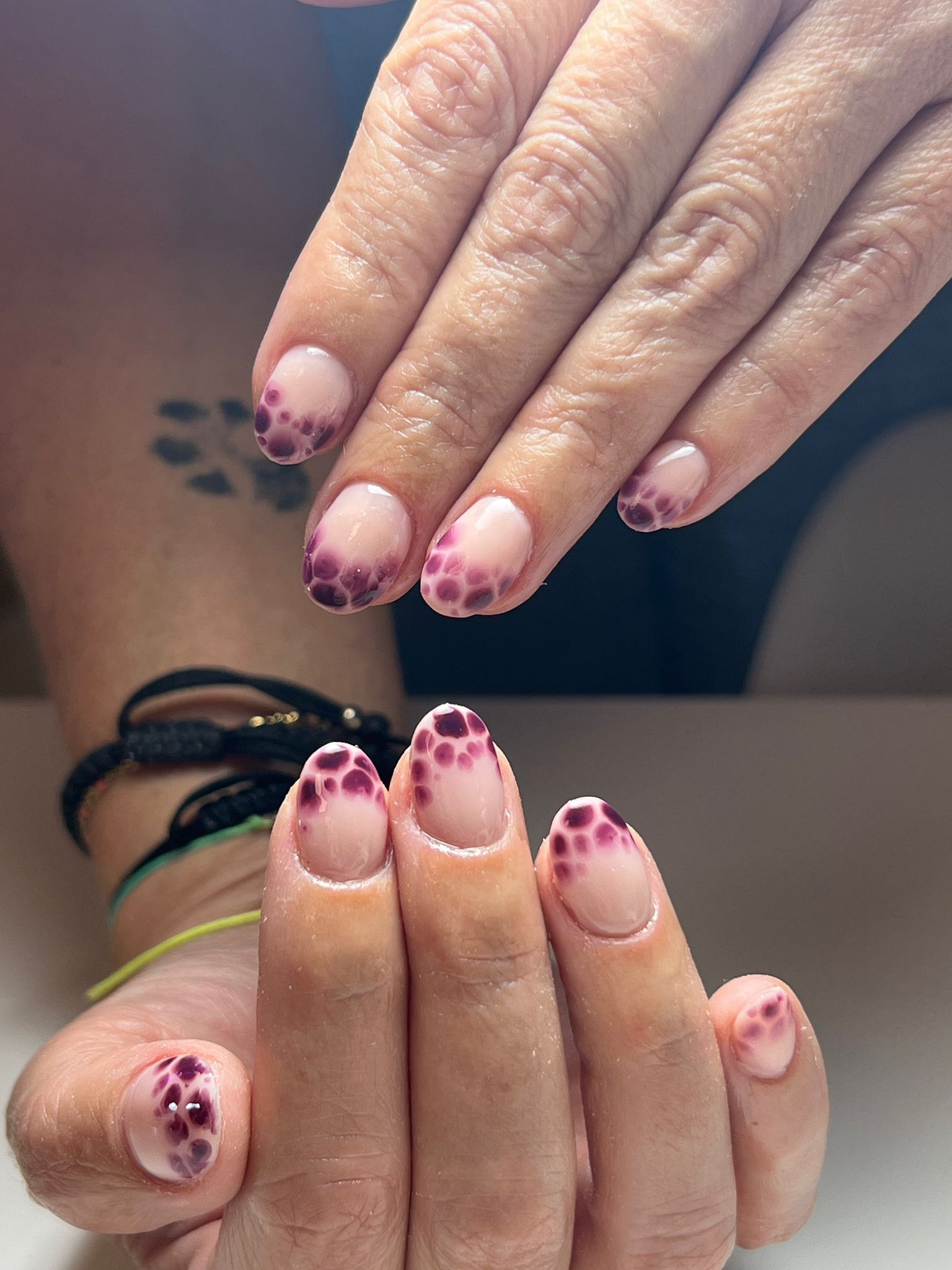 Manos con uñas de forma ovalada, estilo manicura francesa, con puntos de color morado oscuro a lo largo de las puntas.