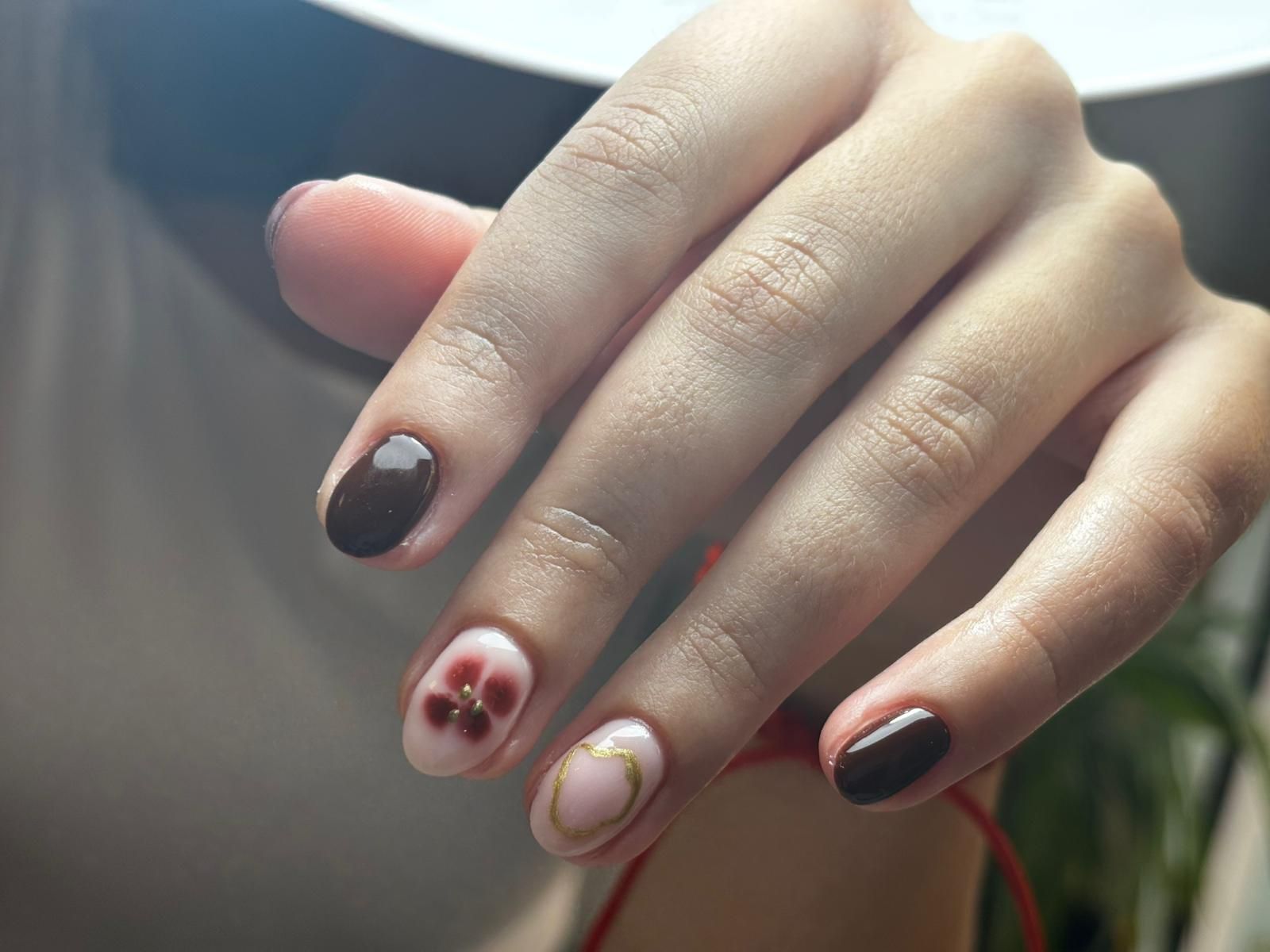 Primer plano de una mano con uñas decoradas con diseños florales y de color marrón.