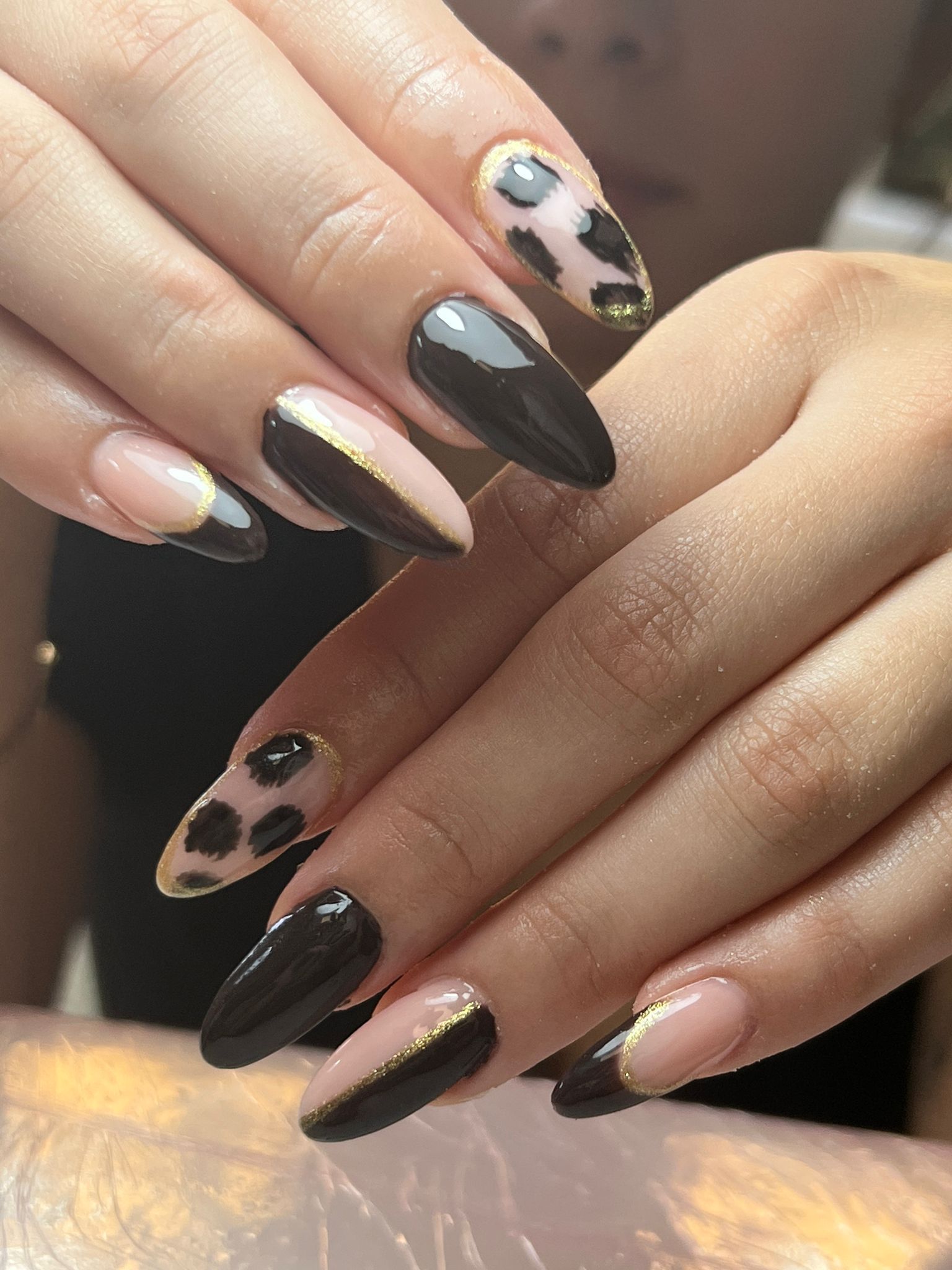 Manos con uñas largas y almendradas. Diseños en negro, nude con detalles dorados y estampado de leopardo.