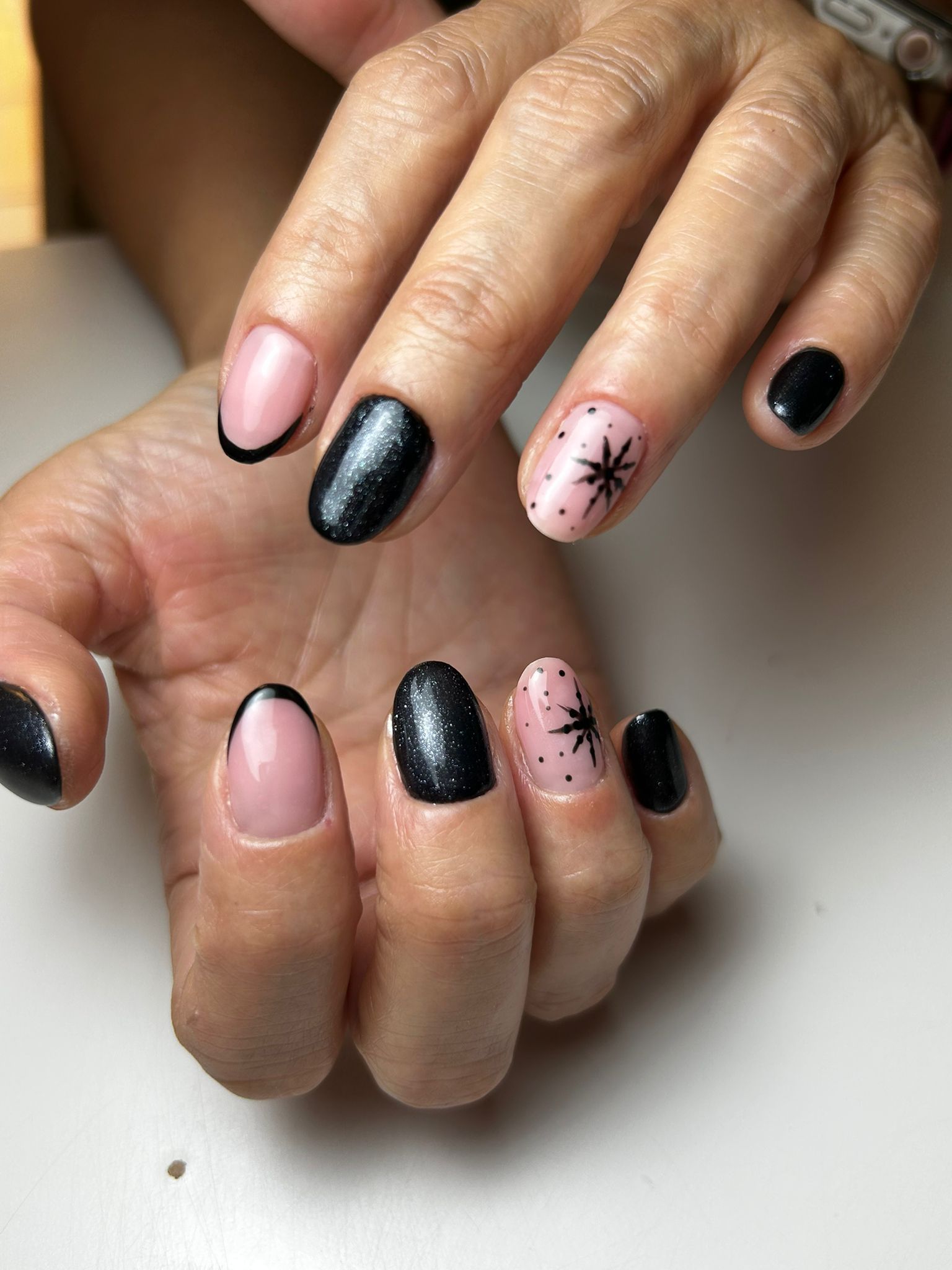 Manos con uñas cuidadas: diseños en negro, rosa y brillo, con acentos de estrellas.