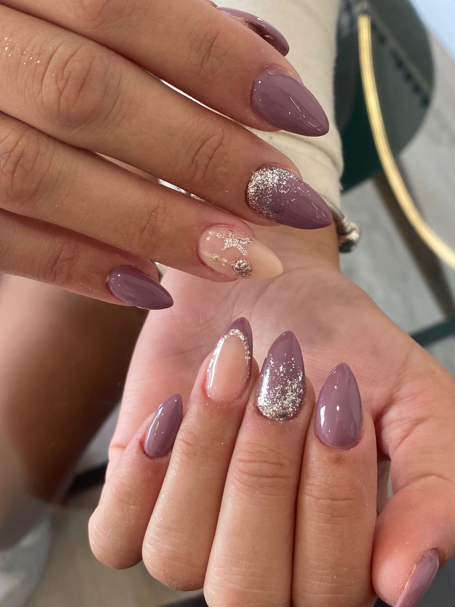 Manos con uñas acrílicas en forma de almendra con purpurina malva y plateada.