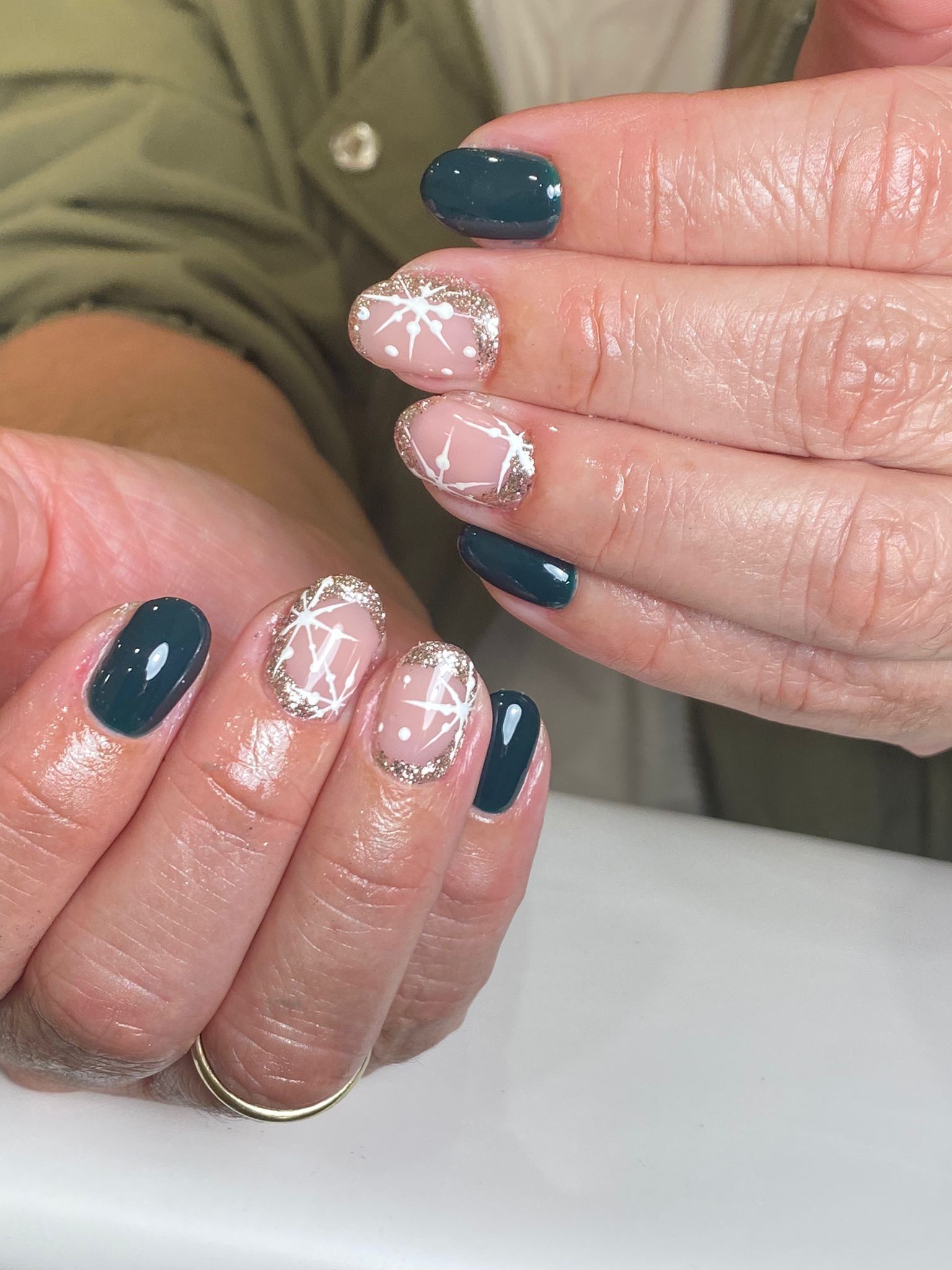 Manos con diseños de uñas en color verde azulado y copos de nieve sobre una base rosa.