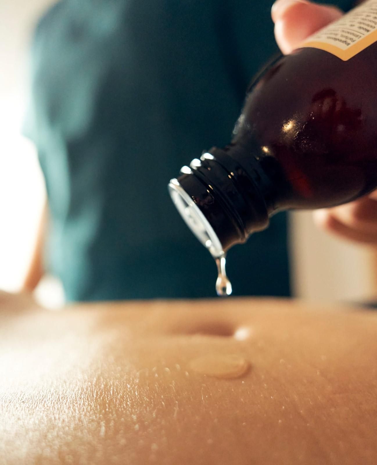 El abdomen de una persona, mientras se vierte aceite de una botella marrón para masajear.