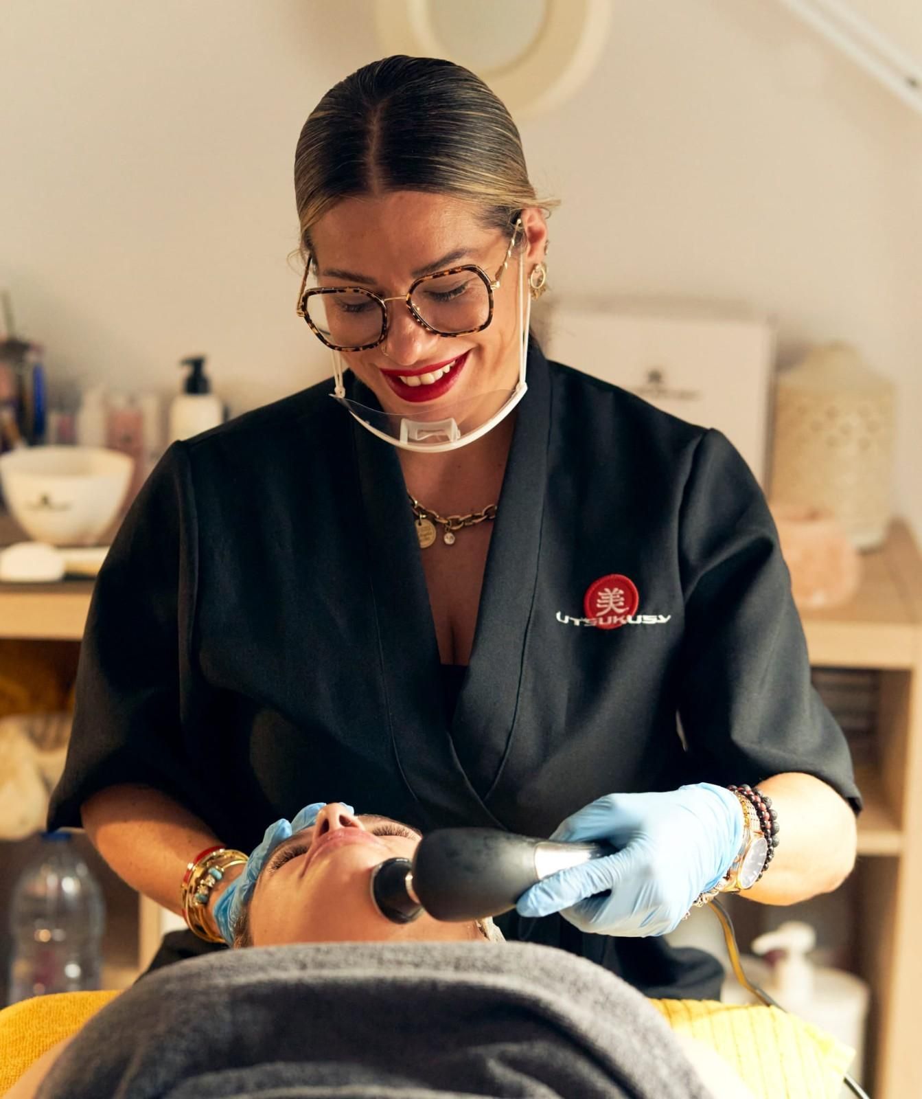Esteticista realizando un tratamiento facial a un cliente con un dispositivo negro.