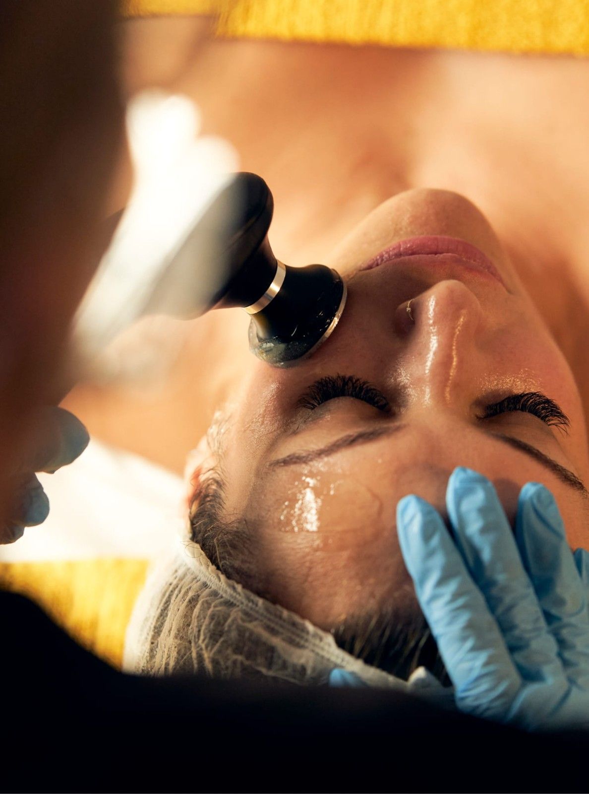 Mujer recibe tratamiento facial; el terapeuta utiliza un dispositivo en su cara, en un entorno de spa.