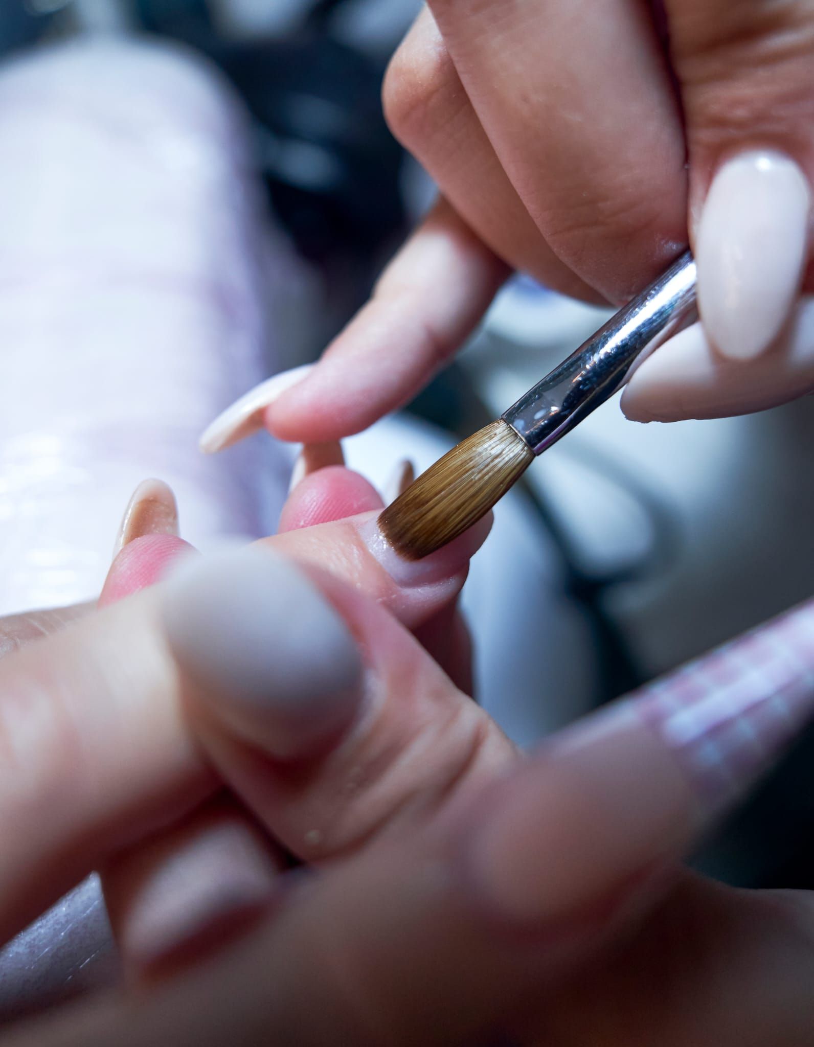 Aplicando esmalte acrílico para uñas con pincel. Primer plano de manos y uñas, esmalte beige.