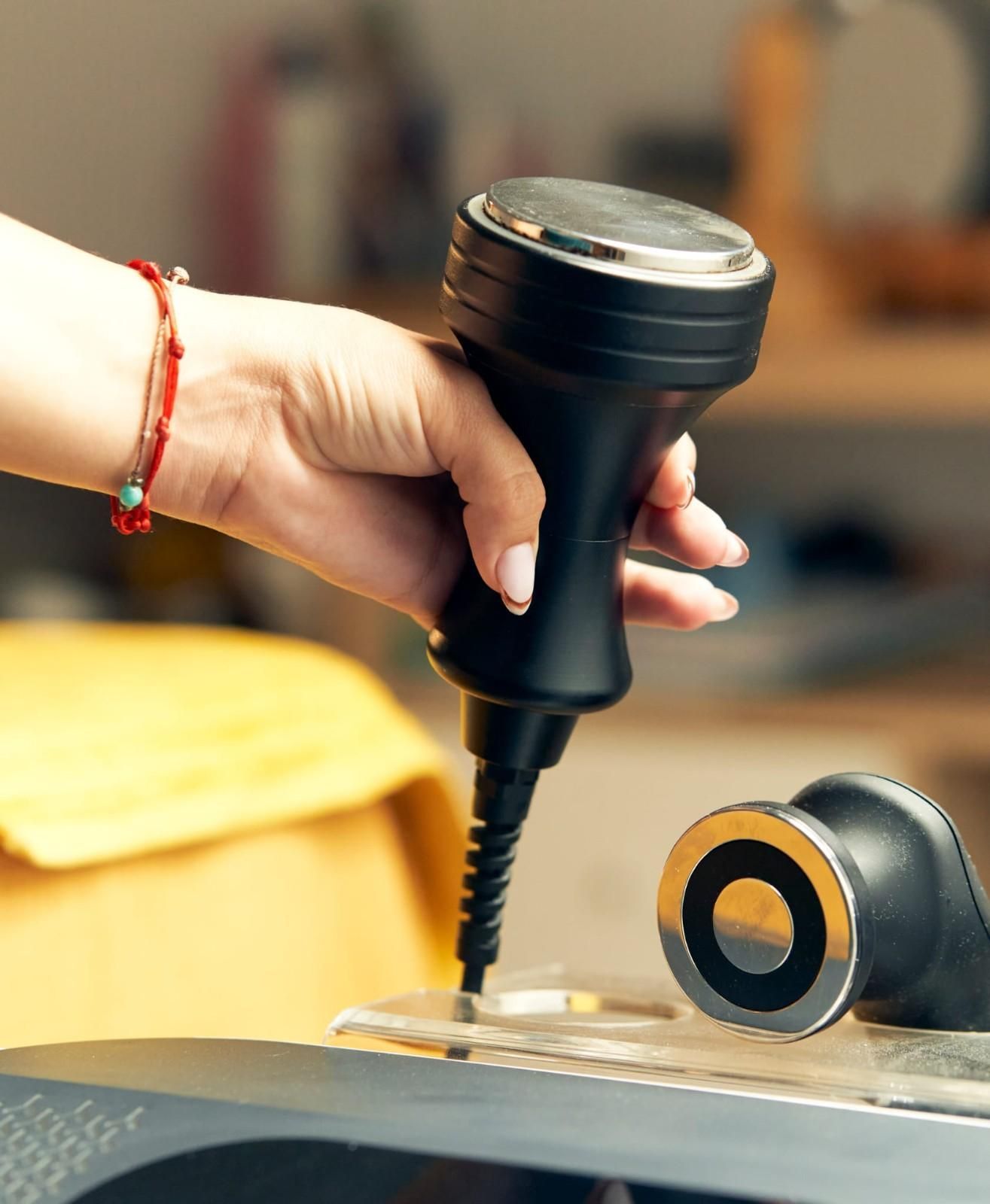 Mano sosteniendo un dispositivo médico negro con borde plateado; otro dispositivo sobre una superficie transparente.
