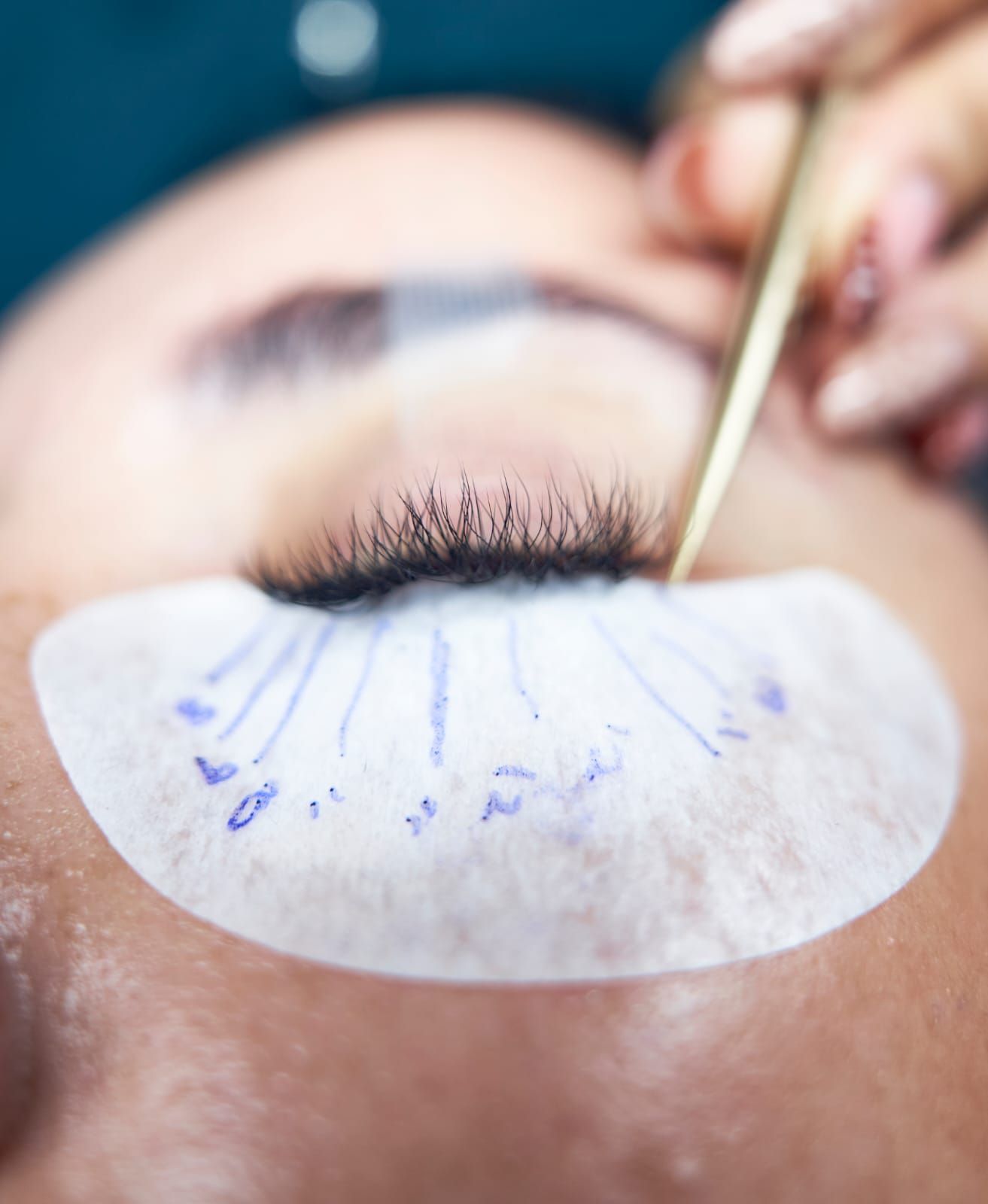 Aplicación de extensiones de pestañas: el ojo de una persona con una almohadilla protectora, pinzas y una mano sosteniéndolas.