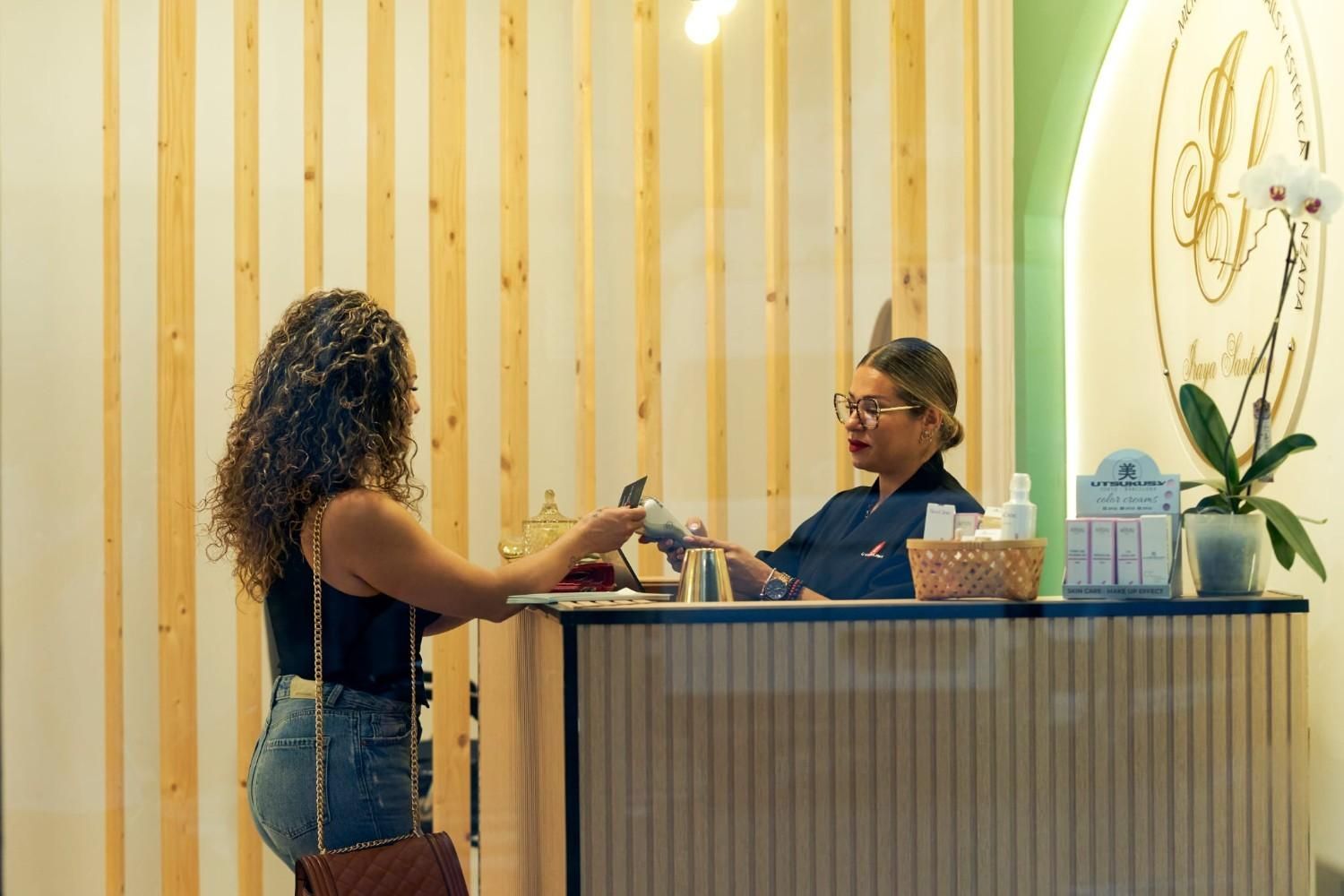 Mujer pagando en el mostrador de recepción del spa con cabello rizado y un recepcionista.