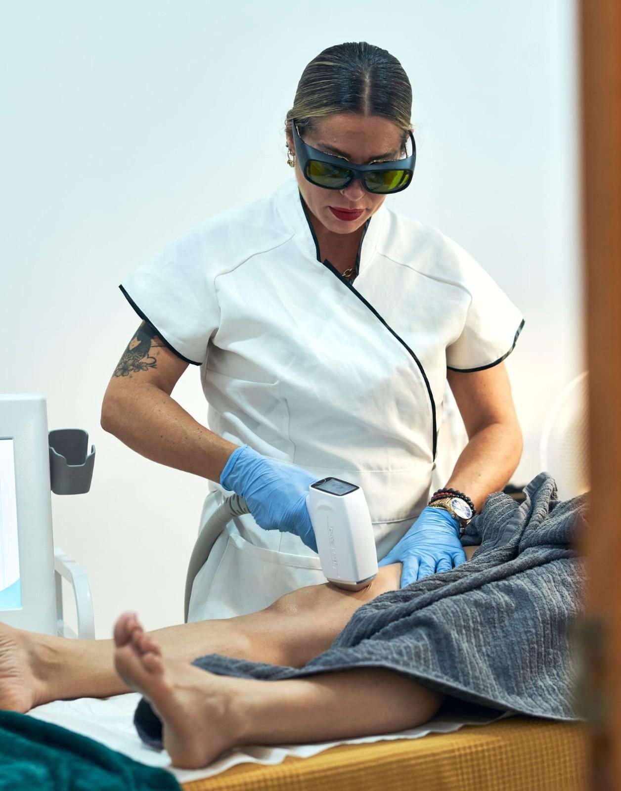 Persona con guantes que utiliza un dispositivo láser en una pierna en un entorno médico.