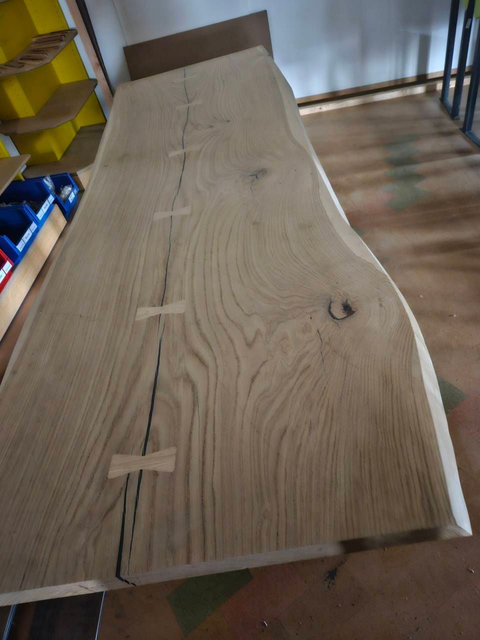 Eine Tischplatte aus Naturholz mit einem langen Riss, der in einer Werkstattumgebung durch drei eingelassene Schmetterlingskeilen stabilisiert wird.