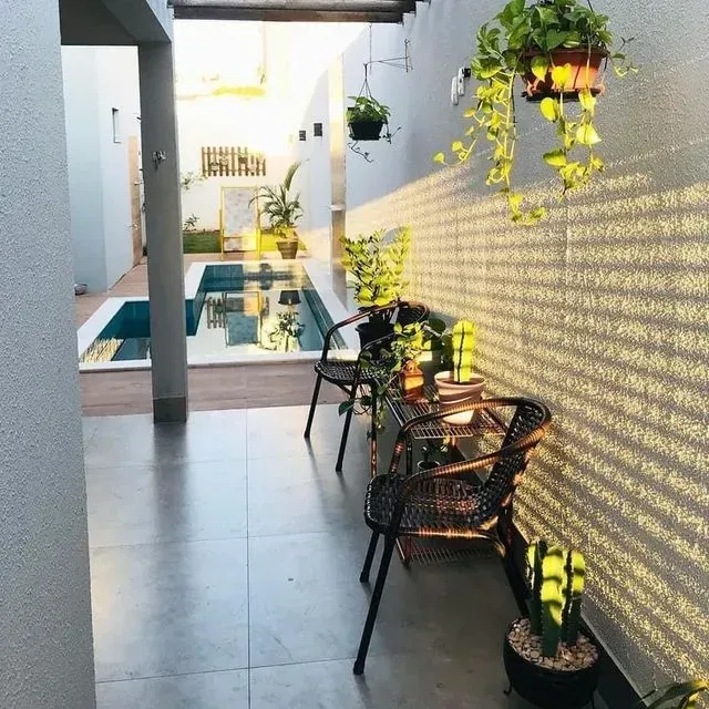 Un patio con sillas y plantas y una piscina al fondo.