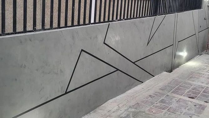 Un muro de hormigón con un diseño geométrico y una valla al fondo.