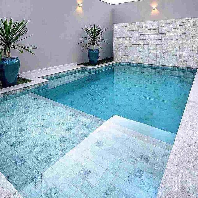 Una gran piscina rodeada de plantas en macetas y un muro de piedra.