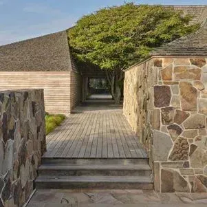 Un muro de piedra rodea una pasarela de madera que conduce a una casa.