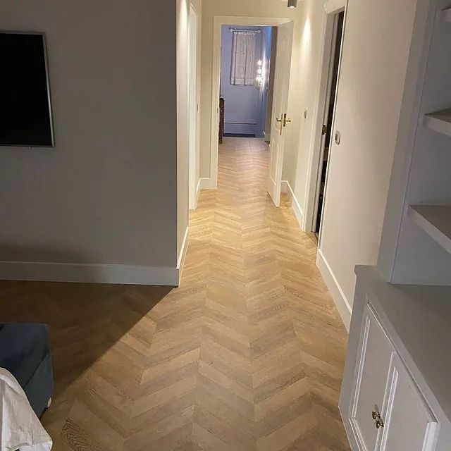 Un pasillo largo con piso de madera y un televisor en la pared.