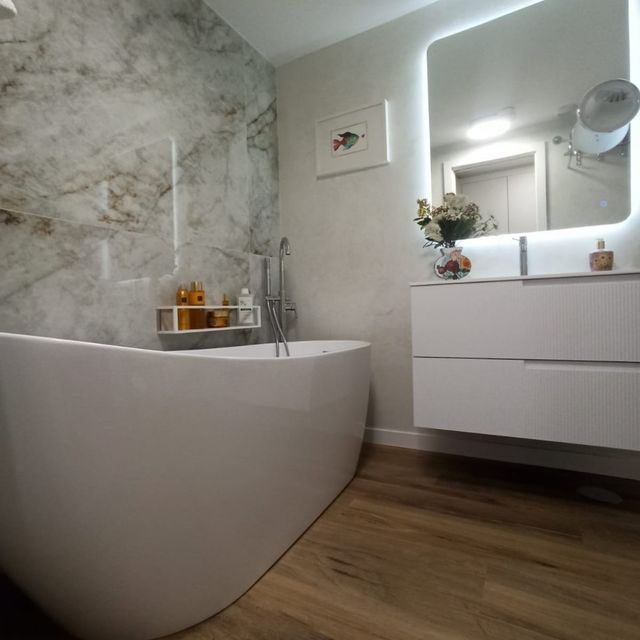 Un baño con bañera, lavabo, espejo y pared de mármol.