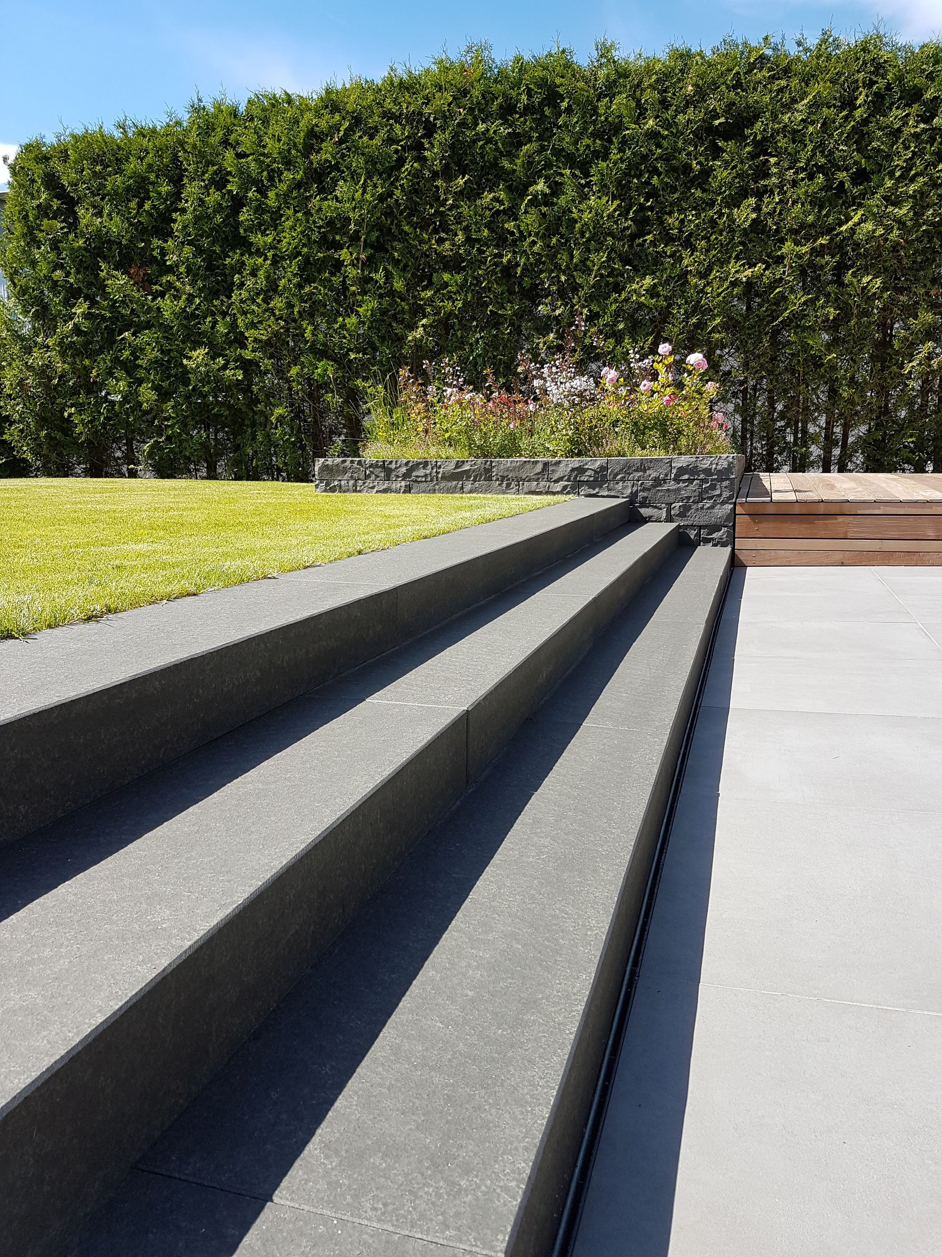 Eine Betontreppe führt hinauf zu einem grünen Rasen mit Hecke und blauem Himmel.
