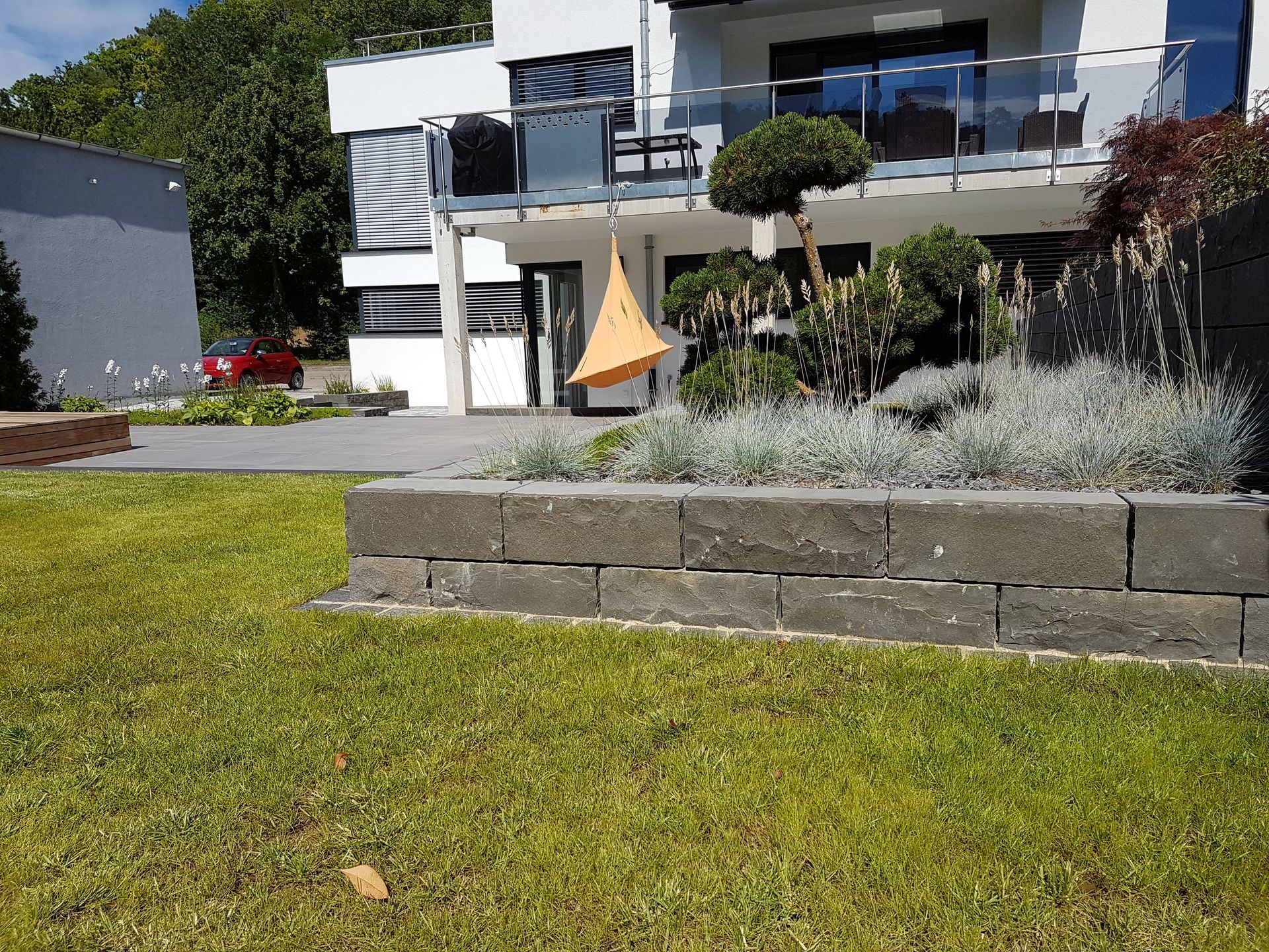 Graue Backsteinmauer vor einem modernen Haus mit grünem Rasen.