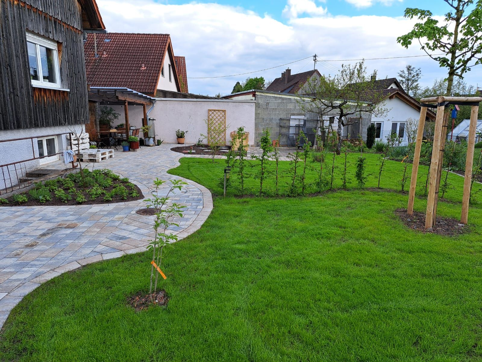 Ein Hof mit einem Steinweg, grünem Gras, einem kleinen Baum und mehreren Gebäuden im Hintergrund.