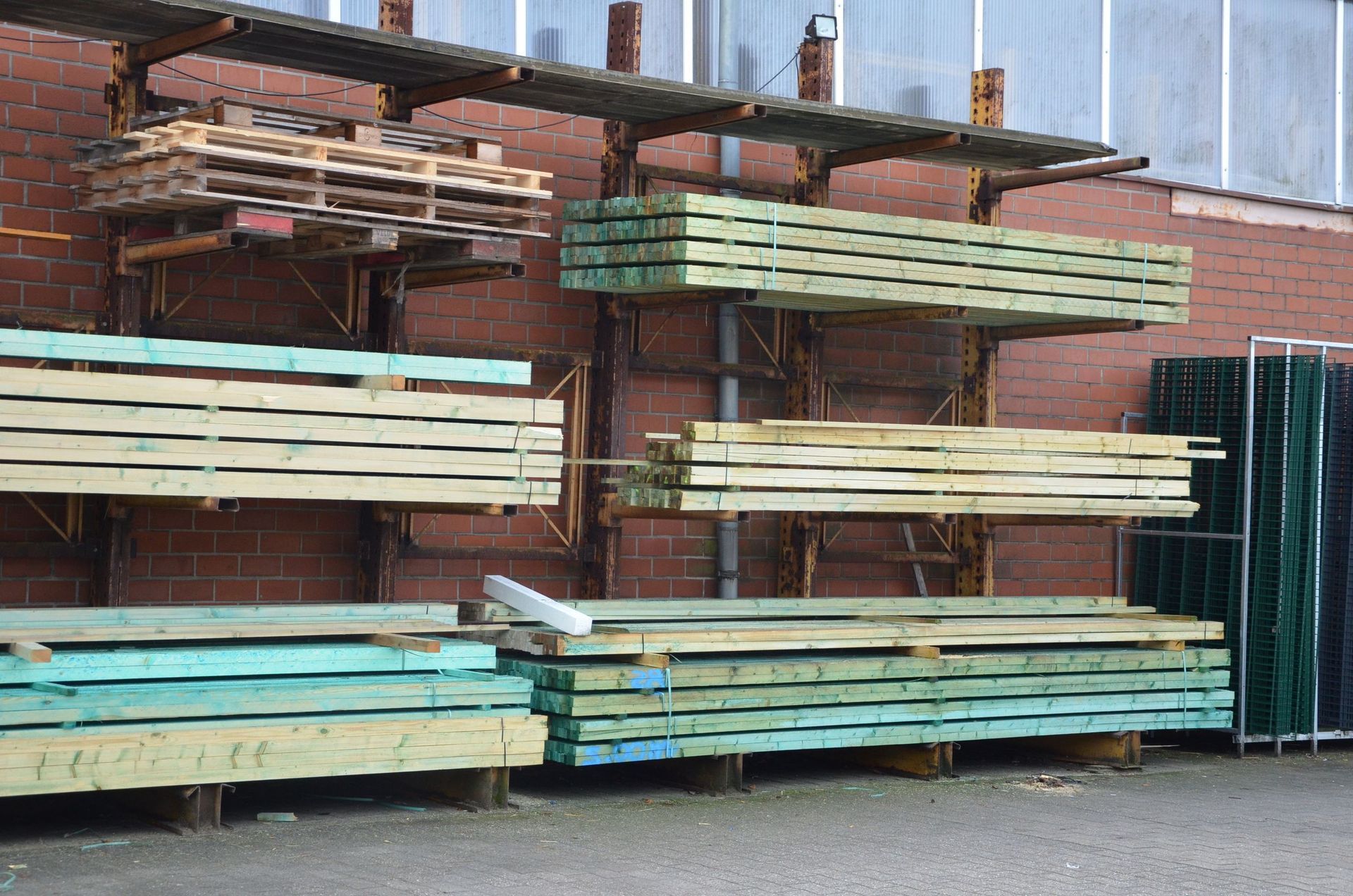 Vor einem Backsteingebäude ist ein Bündel Holz auf einem Gestell gestapelt.