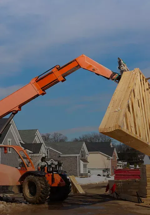Auf einer Baustelle hebt ein Gabelstapler ein großes Stück Holz an.