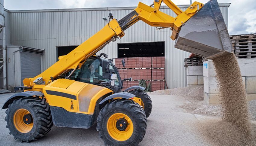 Ein gelber Traktor lädt Sand in einen Eimer.