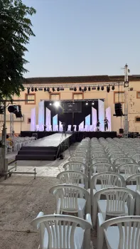 Escenario al aire libre con sillas blancas, luces y fondo, listo para una actuación.