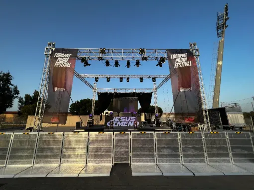 Escenario preparado para un concierto. Incluye iluminación, pancartas y barreras. Cielo azul.