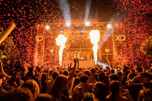 Concierto con escenario, llamas y confeti sobre una multitud de personas.