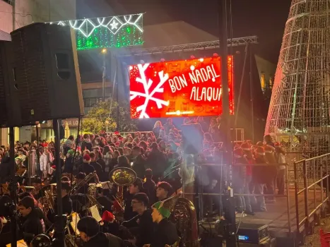 La multitud observa a una banda tocar en un escenario al aire libre por la noche, con una pantalla que muestra 