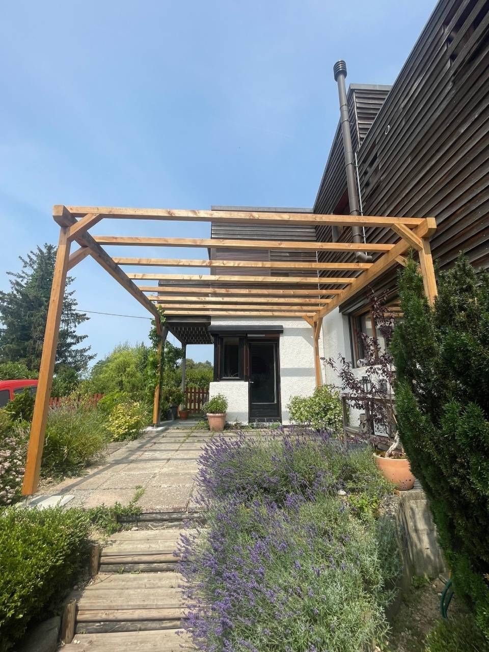 Pergola en bois adossée à une maison de couleur claire.