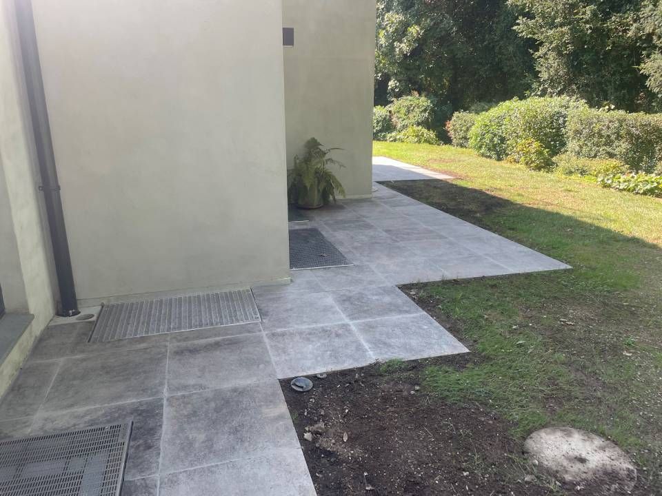 Terrasse carrelée de gris jouxtant un mur clair et une pelouse.