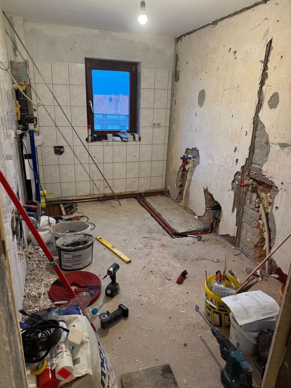 Entkernte Küche mit freigelegten Wänden, sichtbaren Rohren und Baustellenmaterialien wie Eimern und Werkzeugen.