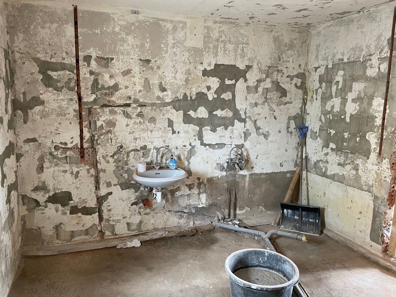 Stark renovierungsbedürftiges Badezimmer mit beschädigten Wänden, alten Sanitäranlagen und Renovierungsmaterialien.