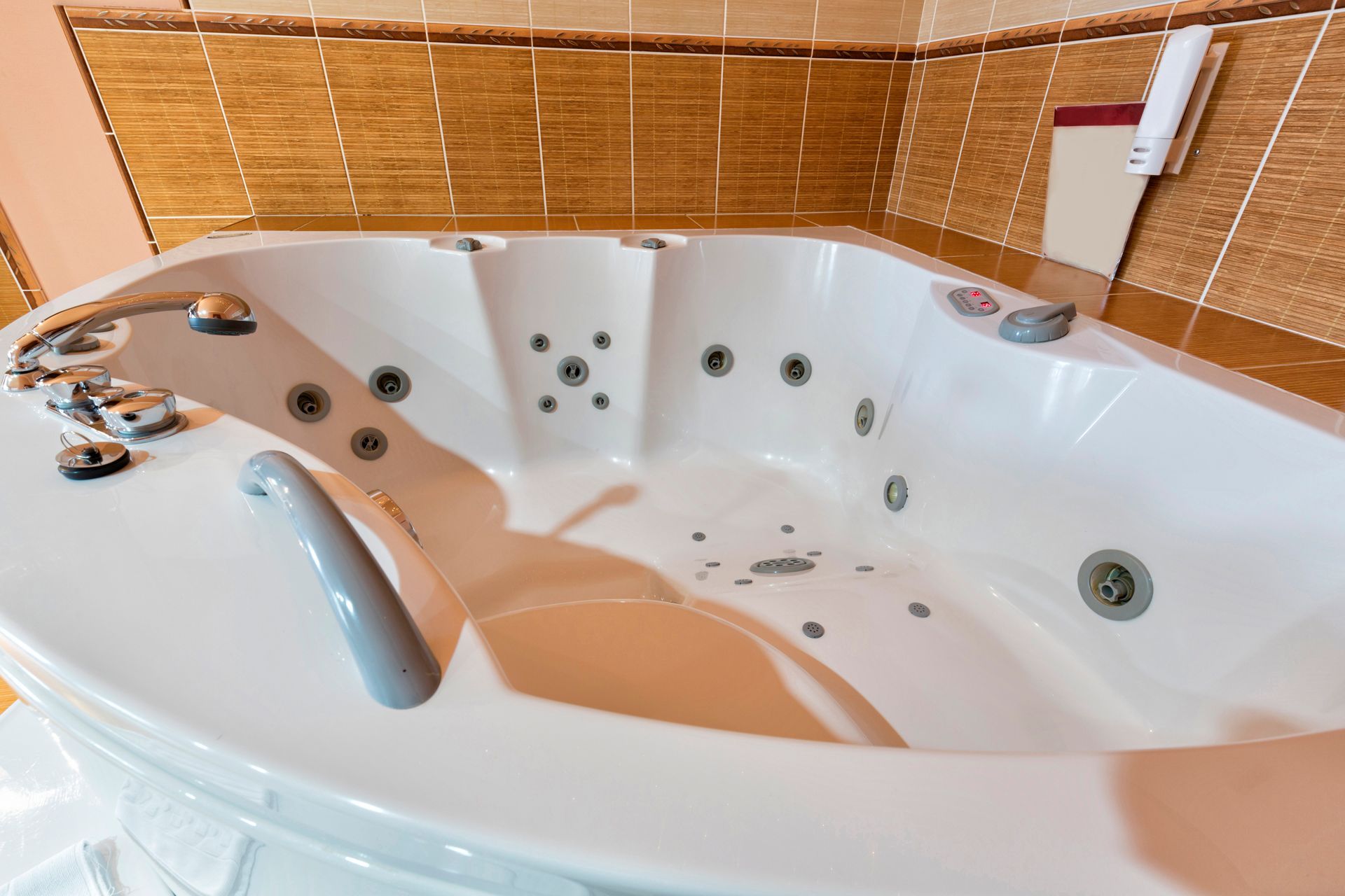 Bañera de hidromasaje blanca en un baño, con varios chorros y pasamanos. Paredes de azulejos al fondo.