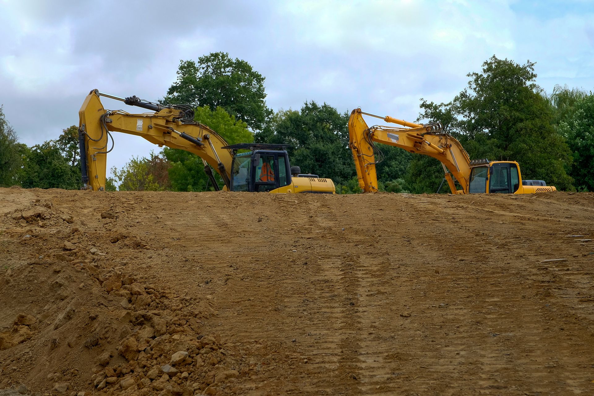 Deux excavatrices jaunes travaillent sur un talus de terre sous un ciel nuageux