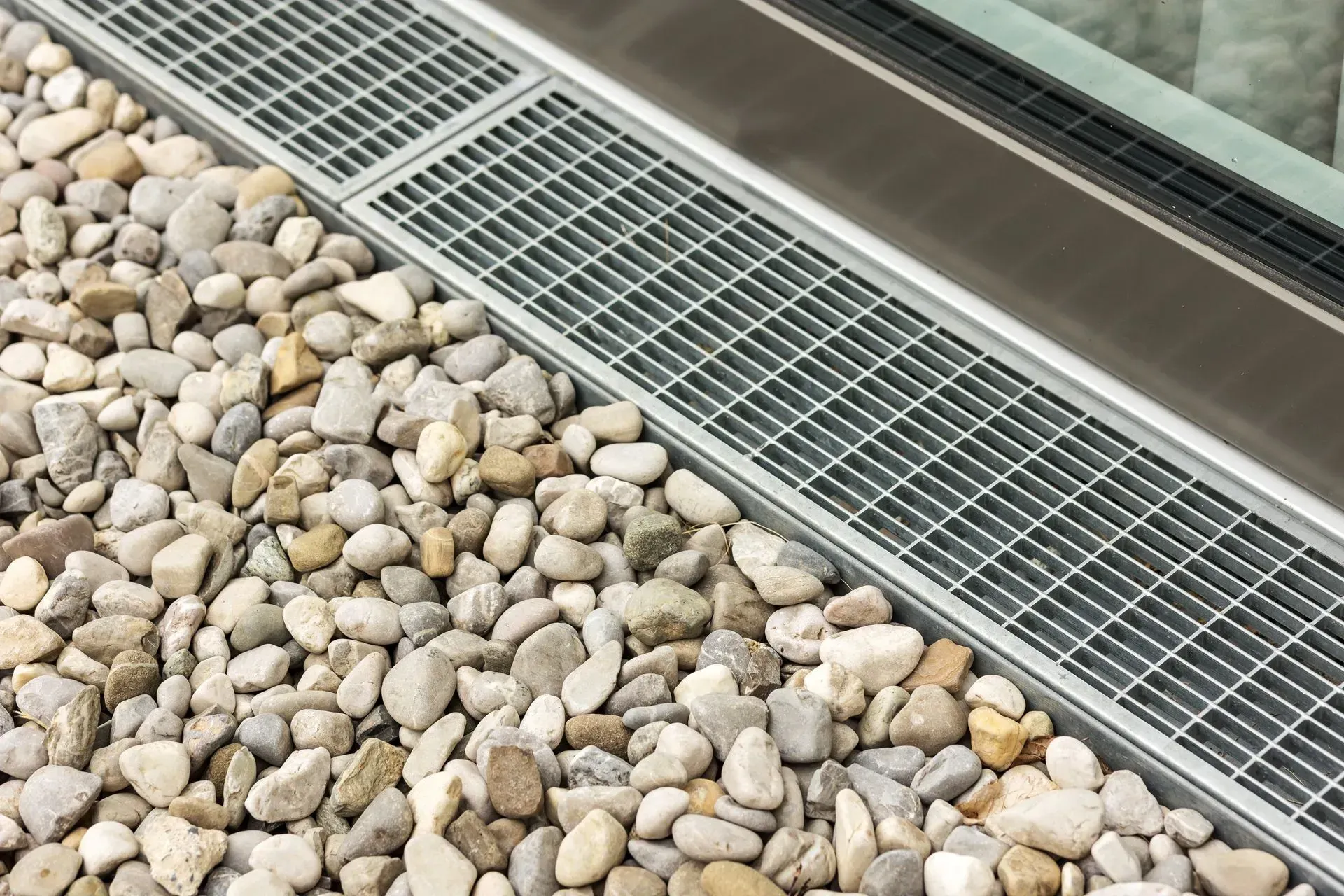 Sol recouvert de cailloux à côté de grilles de drainage métalliques et d'une allée pavée